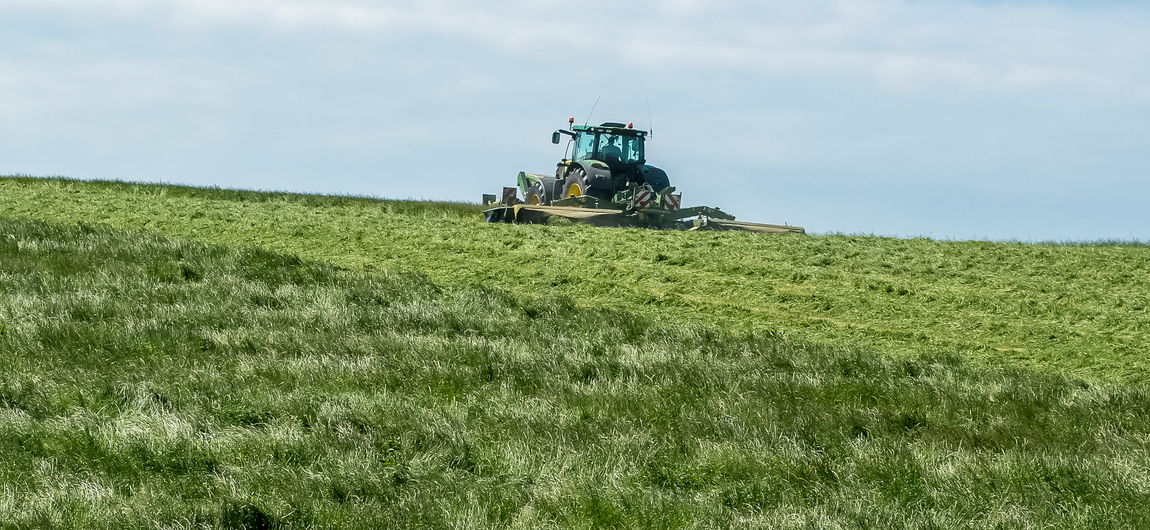 A tractor mowing a field of grass on a hillside